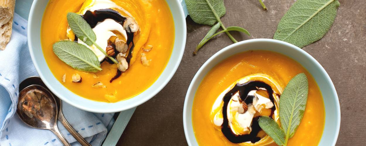 Kürbis-Apfelsuppe in zwei Suppenschalen auf einem Tisch, daneben baguette
