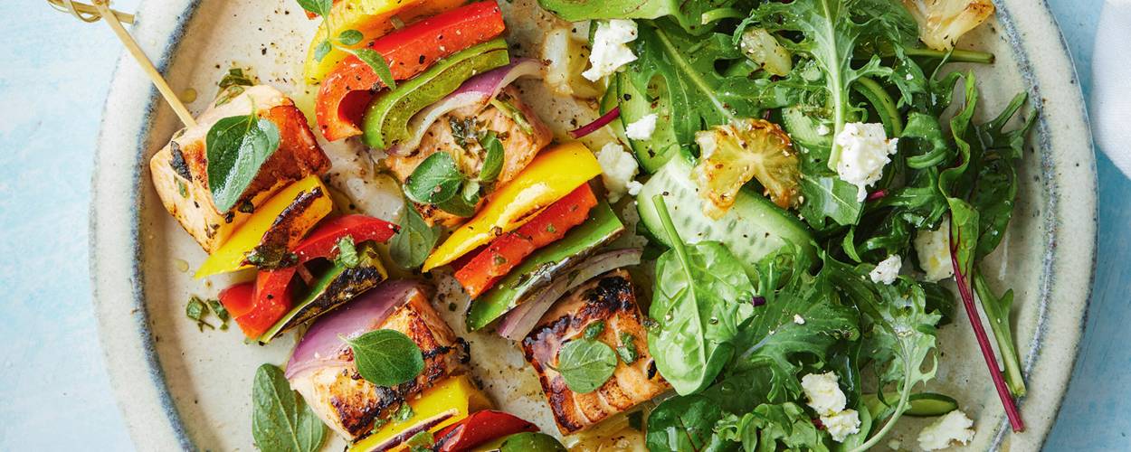 Gegrillte Lachs-Gemüse-Spieße auf einem Teller, daneben Salat und gegrillten Zitronen
