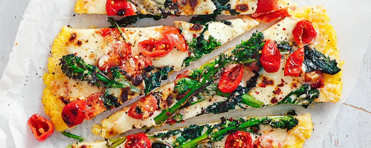 Runde Polentapizza mit Gemüse und Mozzarella in Streifen geschnitten auf einem Teller