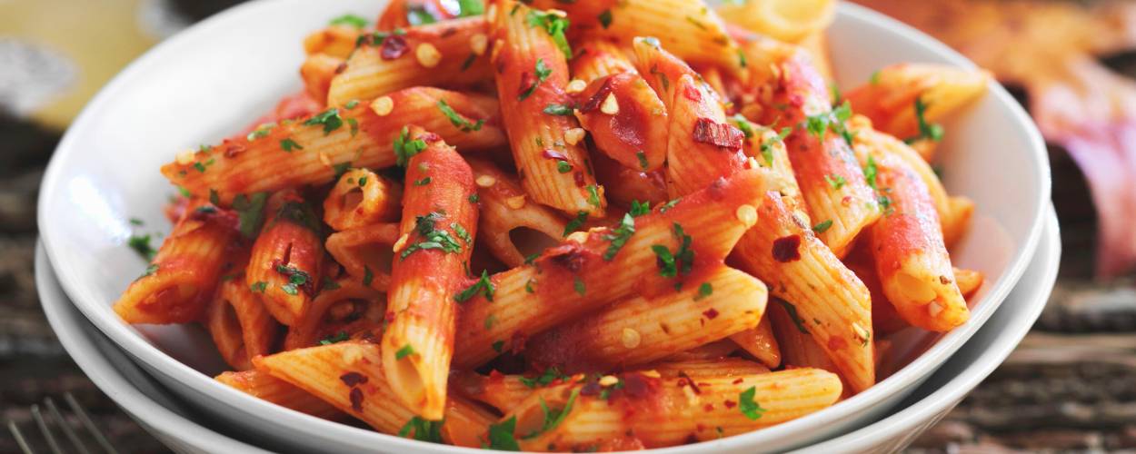 Penne all’arrabbiata in einem tiefen Teller auf einem Tisch, daneben eine Pfeffermühle