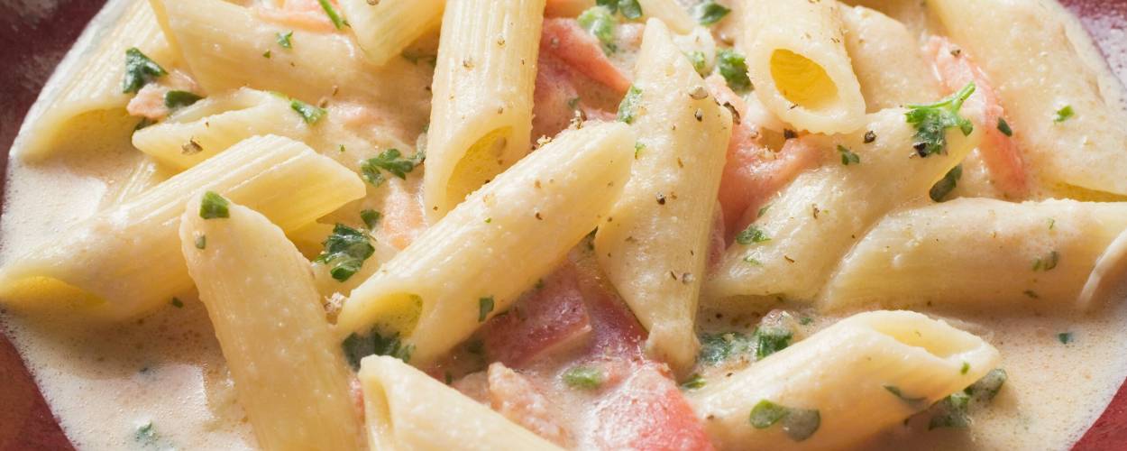 Pasta mit Lachs und Sahnesoße auf einem tiefen Teller, daneben ein Glas Rotwein