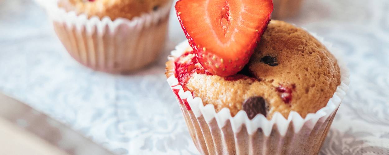 Drei Erdbeer-Muffins dekoriert mit einer halben Erdbeere auf einem Küchentisch