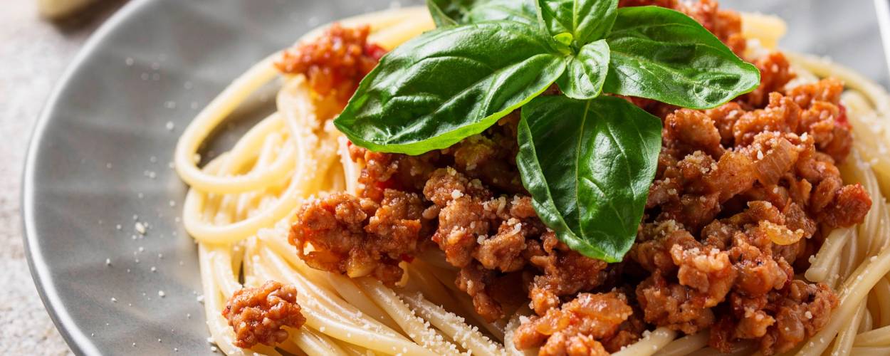 Spaghetti mit Bolognese-Soße auf einem runder Teller getoppt von frischem Basilikum