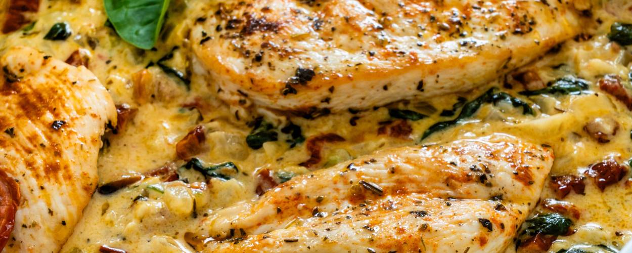 Gebackener Low Carb Toskana Hähnchen-Auflauf mit Spinat und getrockneten Tomaten garniert mit Basilikumblättern in einer Auflaufform