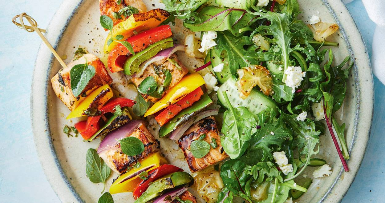 Gegrillte Lachs-Gemüse-Spieße auf einem Teller, daneben Salat und gegrillten Zitronen