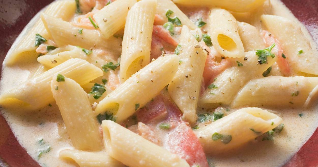 Pasta mit Lachs und Sahnesoße auf einem tiefen Teller, daneben ein Glas Rotwein