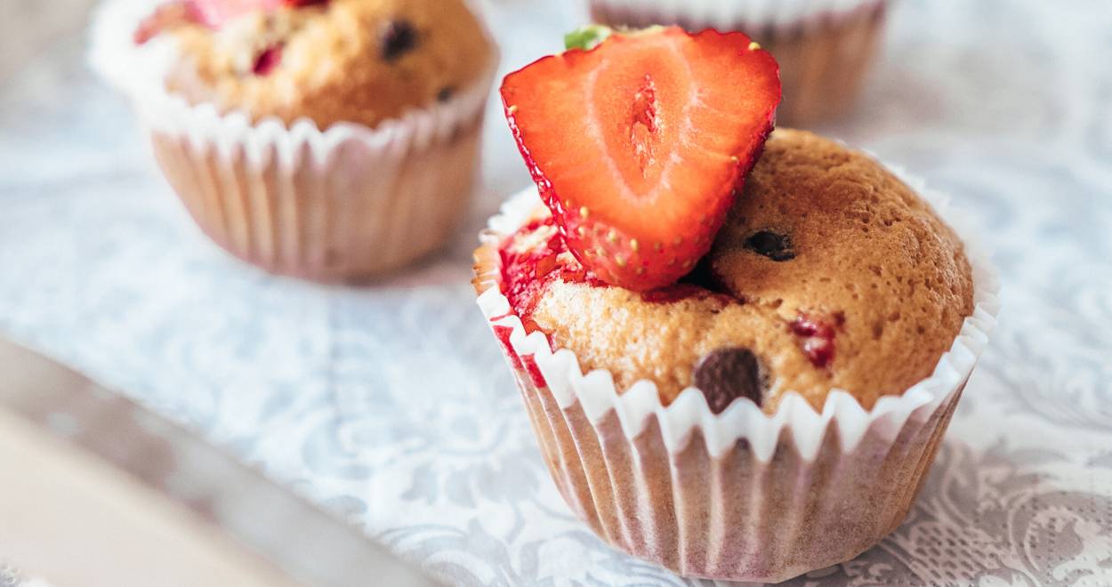 Drei Erdbeer-Muffins dekoriert mit einer halben Erdbeere auf einem Küchentisch
