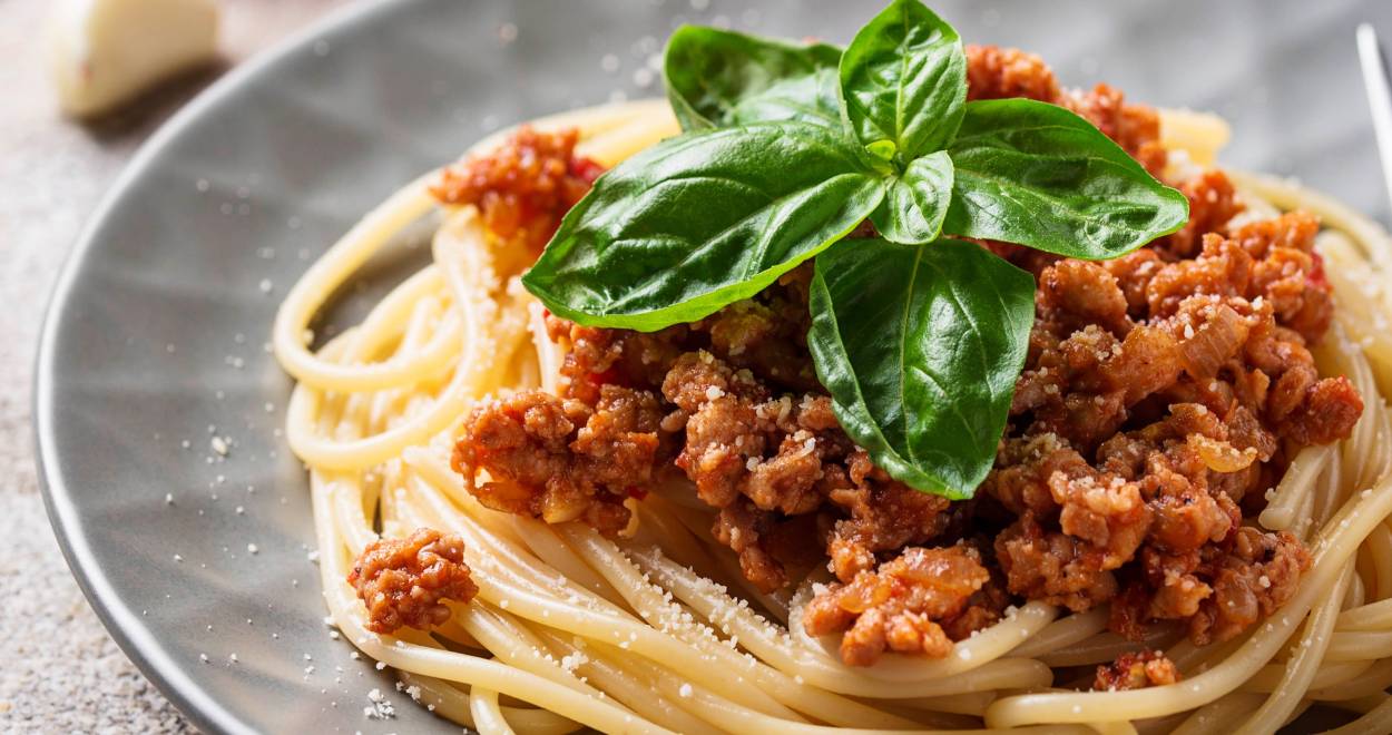 Spaghetti mit Bolognese-Soße auf einem runder Teller getoppt von frischem Basilikum