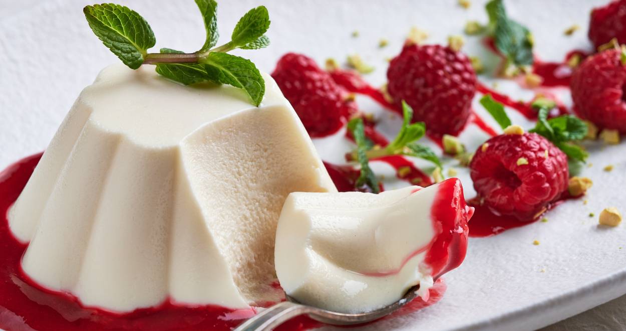 Panna Cotta auf einem Spiegel aus Himbeersoße, daneben frische Himbeeren und Minzblätter