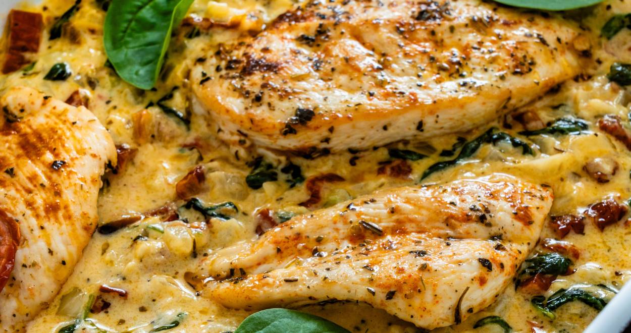 Gebackener Low Carb Toskana Hähnchen-Auflauf mit Spinat und getrockneten Tomaten garniert mit Basilikumblättern in einer Auflaufform