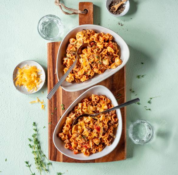 One Pot Pasta mit Bolognese in zwei tiefen Tellern, daneben Käseraspel in einer Schüssel