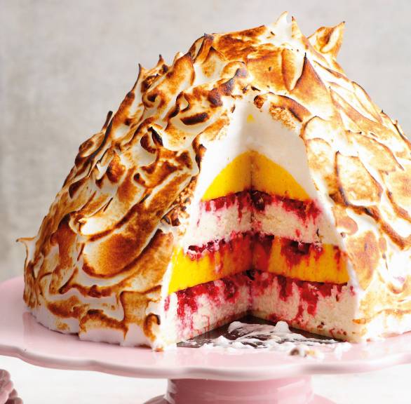 Mango-Kokos-Eisbombe mit Himbeeren und flambierter Baiser-Haube angeschnitten auf einer Tortenplatte