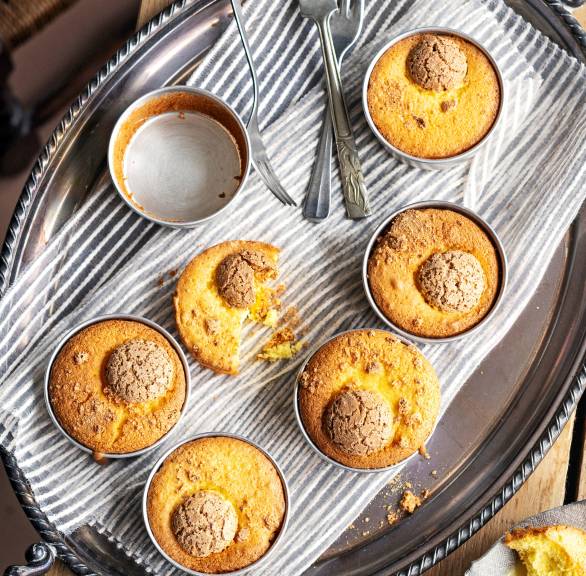 Amaretti-Törtchen in Muffinformen auf einem Tablett, daneben selbst gemachte Vanillesoße auf einem Tisch