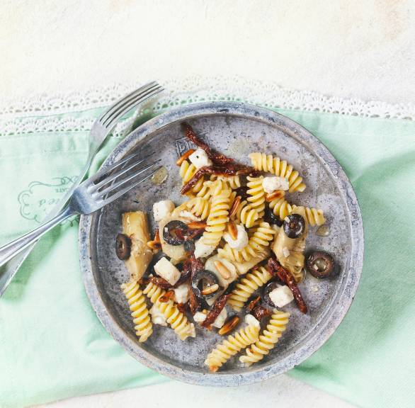 Antipasti-Nudelsalat auf einem Teller getoppt mit Stücken von Büffelmozzarella