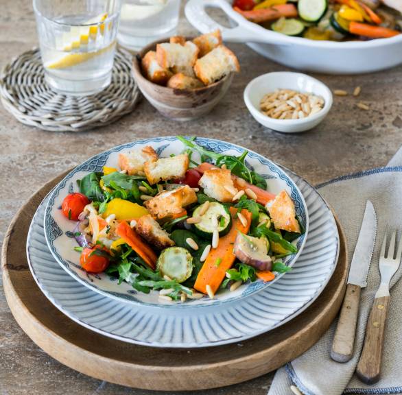 Antipasti-Salat angerichtet auf zwei Teller getoppt mit Croûtons und Pinienkernen