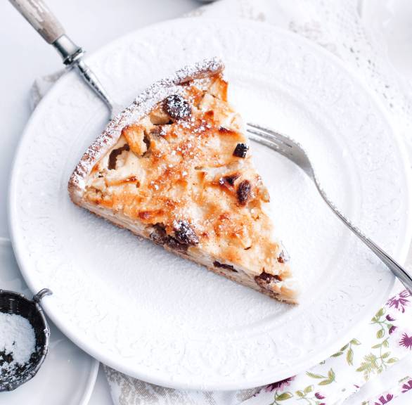 Ein Stück Apfel-Quark-Kuchen mit Rosinen und Mandeln auf einem Kuchenteller