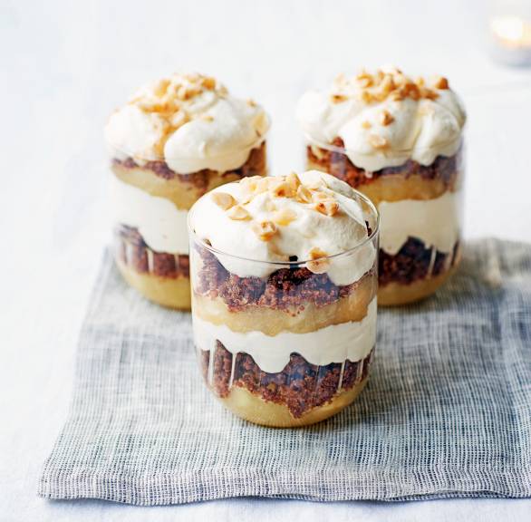 Drei Gläser mit Schichtdessert aus  Apfelkompott, Pumpernickelbröseln und Sahne auf einem Tisch