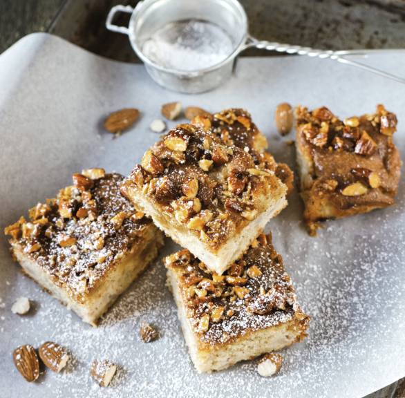 Fünf quadratisch Stücke Apfelkuchen vom Blech mit Zimtmandelhaube auf einem Stück Backpapier 