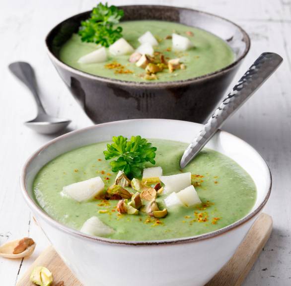Cremige Spinat-Suppe mit Avocado getoppt von Birnenstücken und gehackten Pistazien in zwei Suppenschalen