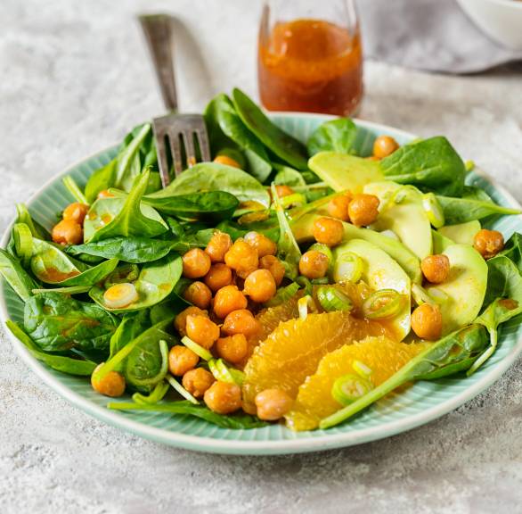 Spinat-Salat mit gebackenen Kichererbsen, Avocadostreifen und  Orangenfilets angerichtet auf einem Teller