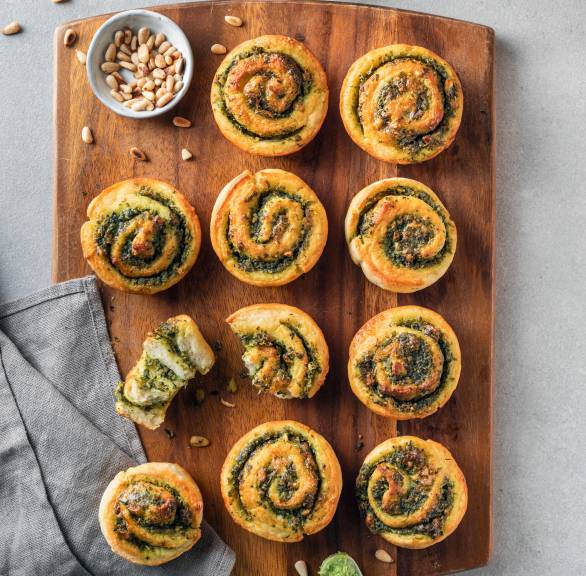 Zehn Bärlauch-Kartoffelbrötchen auf einem Holzbrett, eines davon halbiert von der Seite mit sichtbarer Füllung