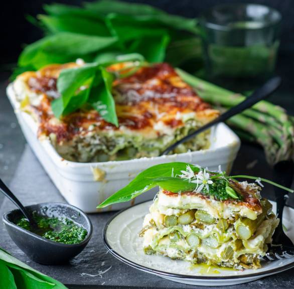 Bärlauch-Spargel-Lasagne in einer Auflaufform, davor ein Stück auf einem Teller