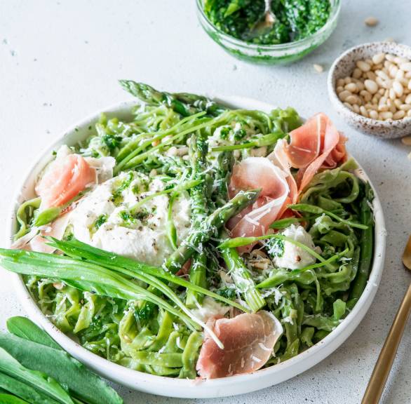Grüne Tagliatelle mit Bärlauchpesto, grünem Spargel, Mozzarlla und Parmaschinken in einem tiefen Teller