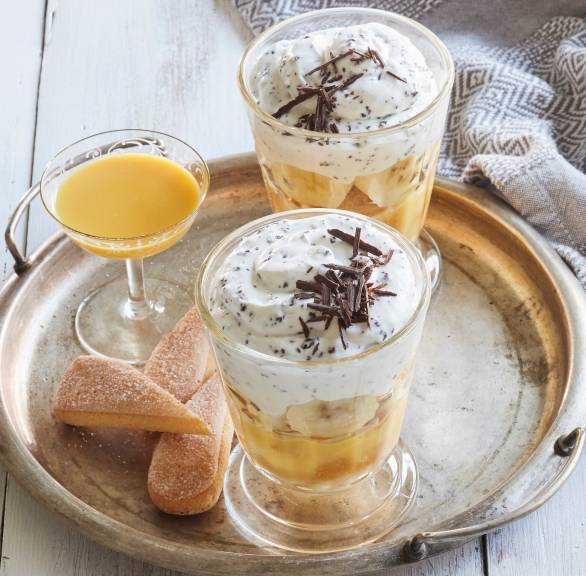 Bananentiramisu in zwei Gläser geschichtet, daneben ein Glas Eierlikör auf einem Tisch