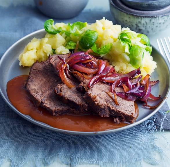 Scheiben von Rinderbraten auf einem Teller mit Sauce bedeckt, daneben Kartoffelpüree und Rosenkohl