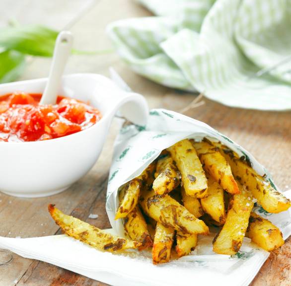 Kartoffelsticks in einer Papiertüte auf einem Holztisch, daneben Salsa und Basilikum