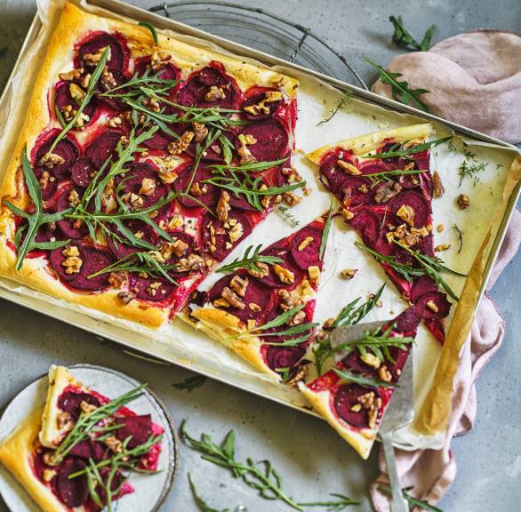 rechteckige Blätterteig-Pizza mit Rote Bete, Rucola, Ziegenkäse und Walnüssen angeschnitten auf einem Backblech