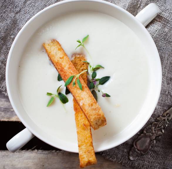 Blumenkohlcremesuppe garniert mit Brotsticks und frischen Kräutern in einer Suppenschale