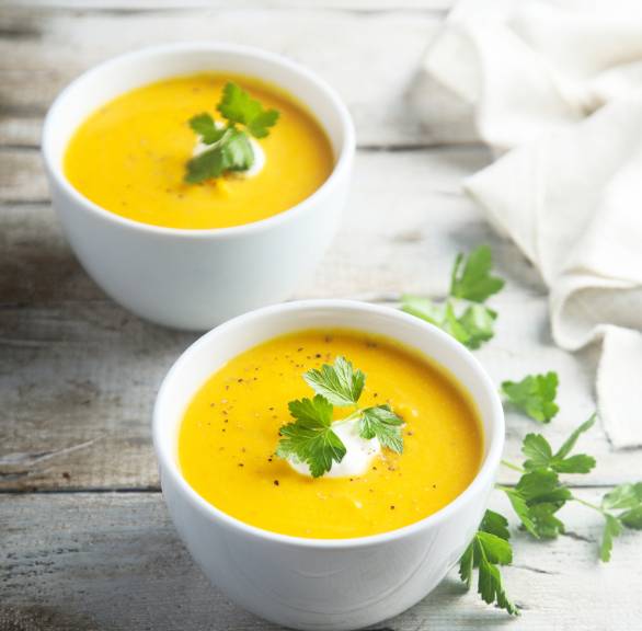 Gelbe Blumenkohlsuppe in zwei Schalen garniert mit frischen Kräutern auf einem Tisch