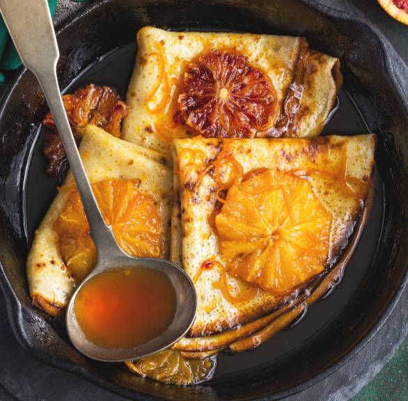 Mehrere gefaltene Crespelle auf einem Dessertteller getoppt von mit Blutorangenscheiben und Amaretto-Sauce