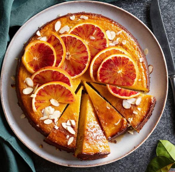 Runder glutenfreier Mandel-Kuchen belegt mit Blutorangenscheiben angeschnitten auf einer Kuchenplatte