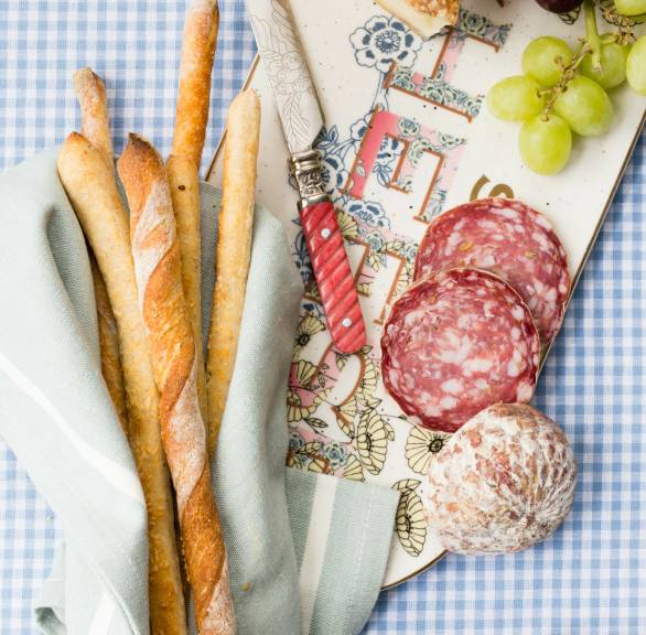 Selbstgebackene italienische Brotsticks auf einer Snackplatte mit Käse, Weintrauben und Salami