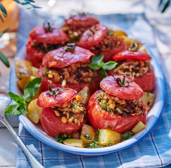 Gebackene, vegan gefüllte Tomaten auf einer Servierplatte umgeben von Kartoffeln aus dem Ofen