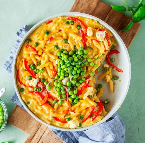Pfanne mit Frittata mit Feta, Nudeln und Paprika getoppt von Erbsensalat auf einem Holzbrett