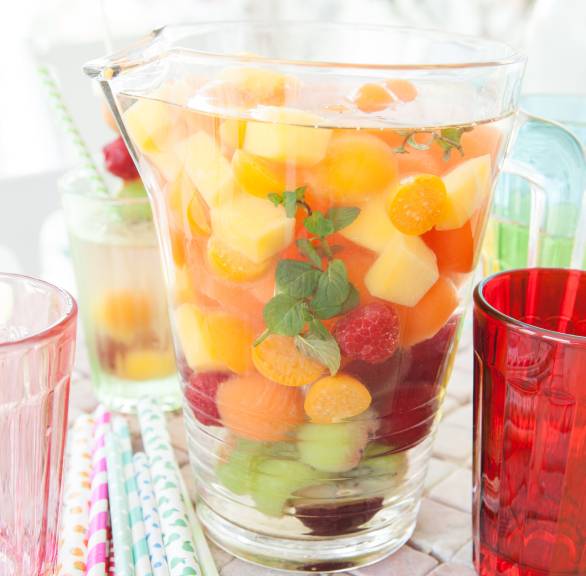 Bowle in einer Karaffe voll mit Früchten auf einem Gartentisch, daneben Papierstrohhalme