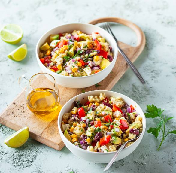 Couccous-Salat in zwei Salatschüsseln mit Avocado und Feta getoppt, daneben Dressing