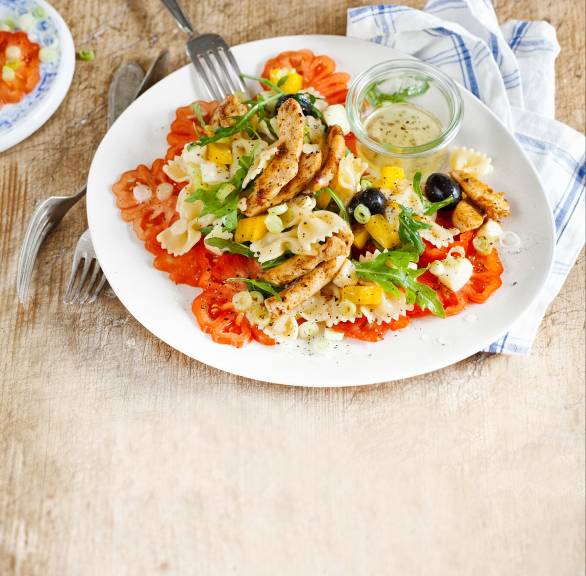 Nudelsalat getoppt mit Hähnchentreifen und Mozzarella auf einem Tisch