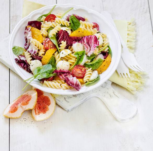 Nudelsalat aus Fusilli , Spinat und Tomaten in einer Schüssel getoppt mit Mozzarellakugeln und Grapefruitstücken auf einem Tisch