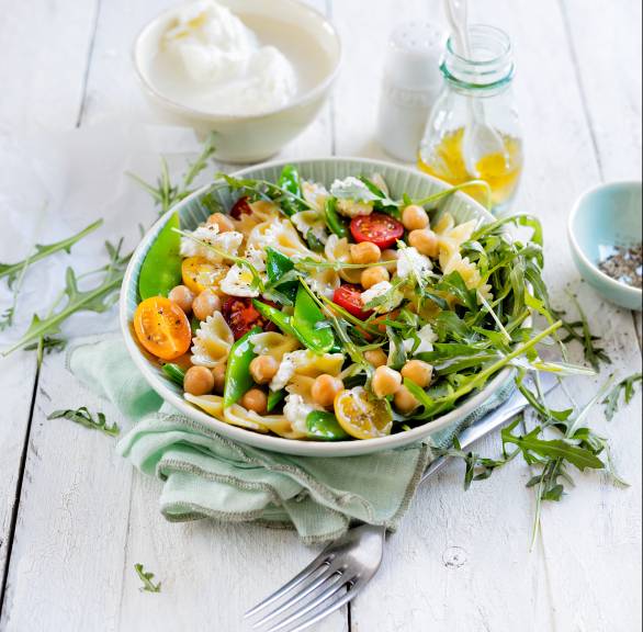Pastasalat aus Fusilli in einer Salatschüssel getoppt mit Mozzarella und Kichererbsen auf einem Tisch