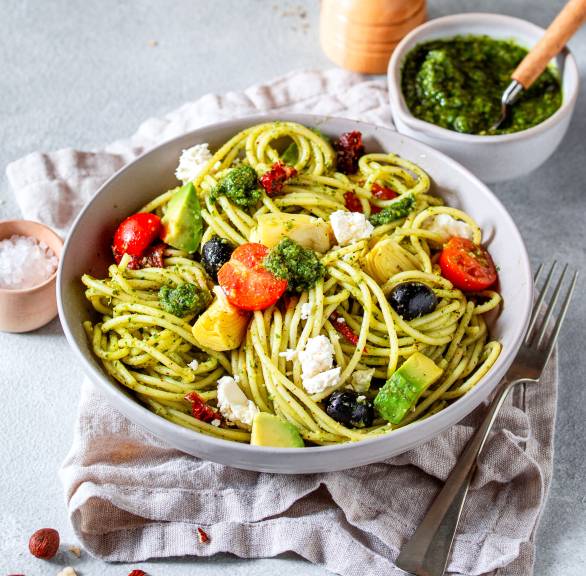 Spaghettisalat auf einem tiefen Teller, daneben eine Schale mit Bärlauchpesto und eine Pfeffermühle