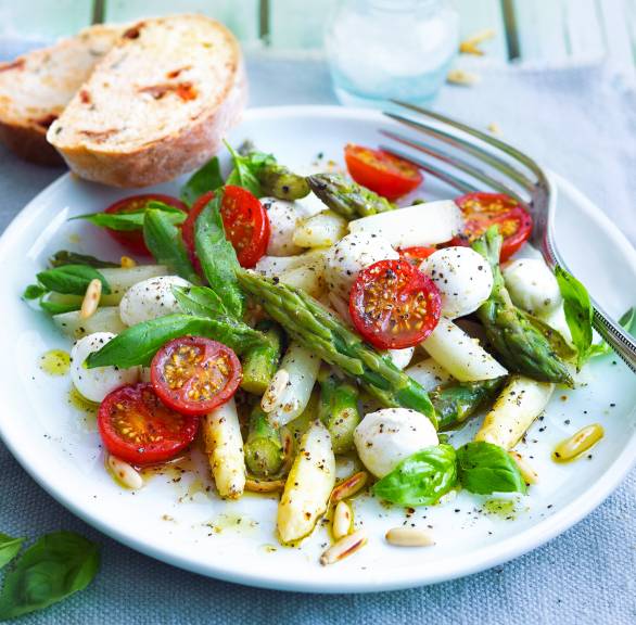 Spargelsalat mit grünem und weißem Spargel, Tomaten und Mozzarella auf einem Teller, daneben selbstgebackene Ciabatta