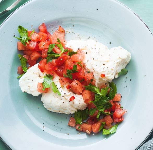 Zerteilter Burrata auf einem Teller getoppt von Tomaten-Wassermelonen-Salsa auf einem Teller