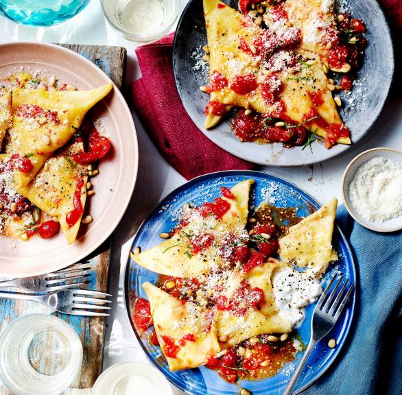 Dreieckige Pansotti auf mehreren Tellern, Füllung aus geschmolzenem Burrata tritt heraus, darauf Kirschtomaten, Parmesan und Basilikum