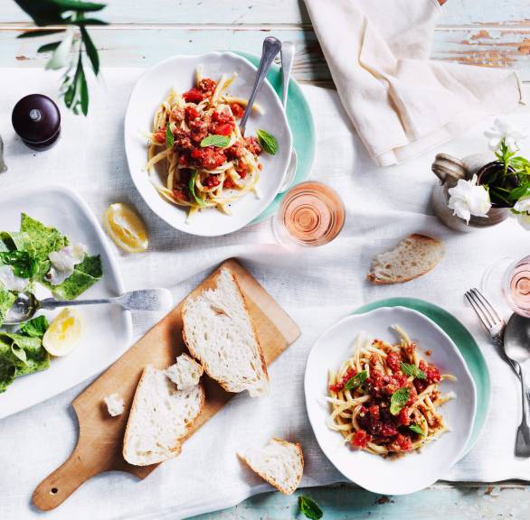 Busiate-Nudeln angerichtet auf zwei Tellern getoppt mit grünem  Pesto Trapanese auf einem Tisch mit Salat und Brot