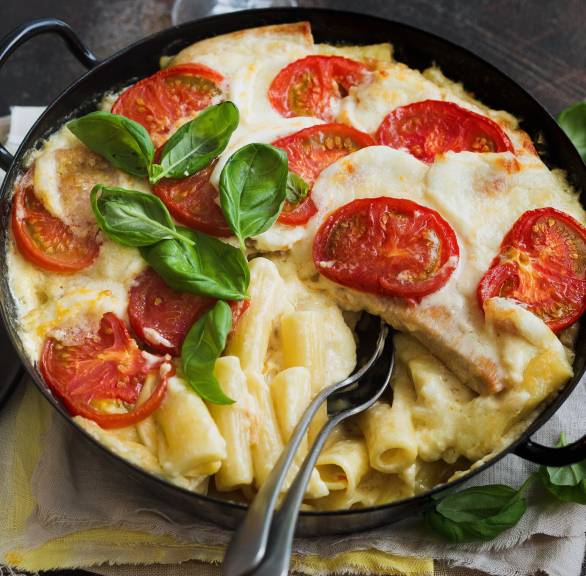 Auflauf aus Nudeln und Putenschnitzel getoppt von Tomatenscheiben und Mozzarella auf einem Tisch