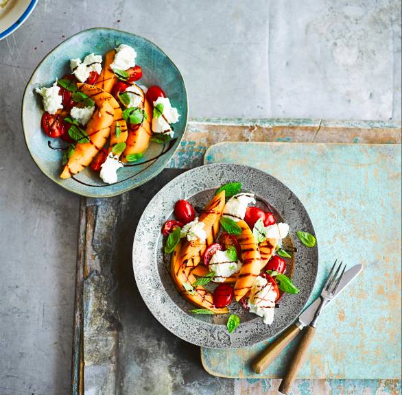 Caprese-Salat in zwei Salattellern getoppt mit Mozzarella und gegrillter Melone auf einem Tisch